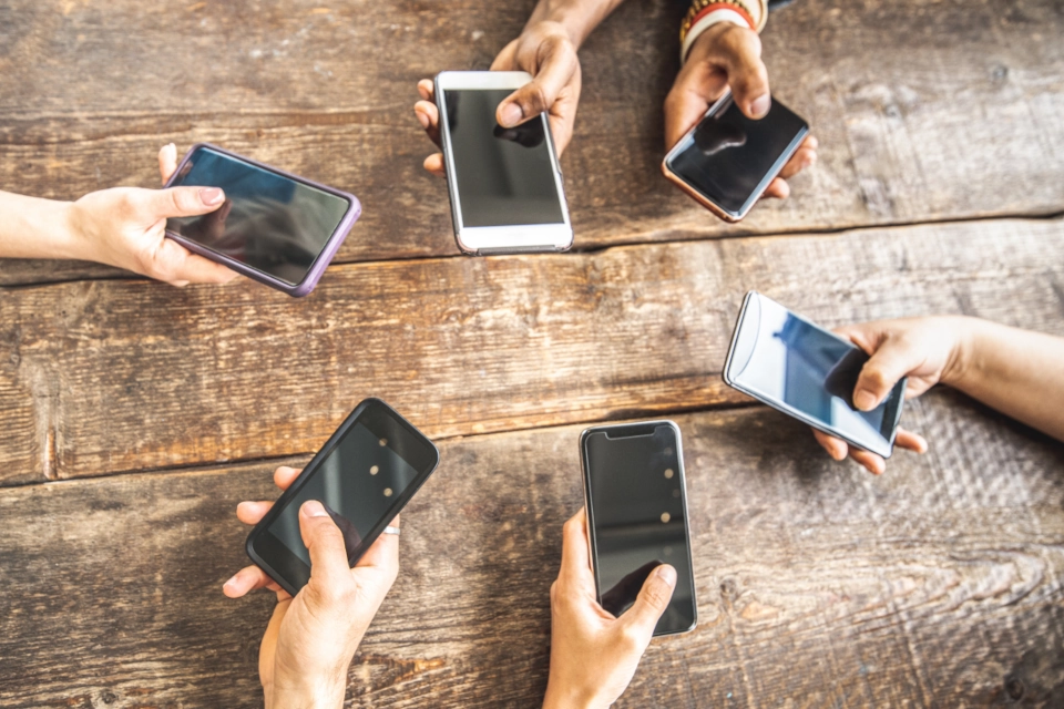 Circle of hands holding smartphones on a wooden table