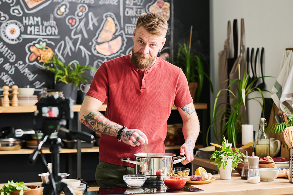 bearded food influencer cooking something in a pot in a stylish kitchen
